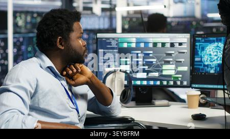 Server room engineer in wheelchair and colleague oversee automated tasks working with node tree programming tool. Stock Photo