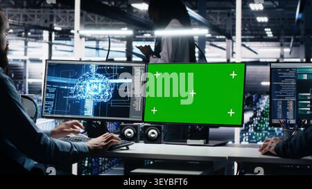 Data center technician monitors operational metrics on green screen PC inside a server room to improve infrastructure performance. Stock Photo