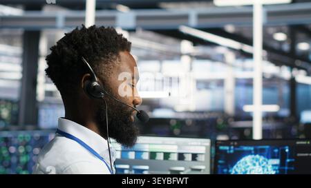 Server room employee talking in headset mic, coordinating technicians setting up hardware for AI deployment. Stock Photo