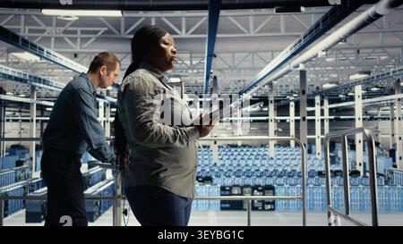 IT expert checks server environment activity working with digital tablet while walking on industrial platform. Stock Photo