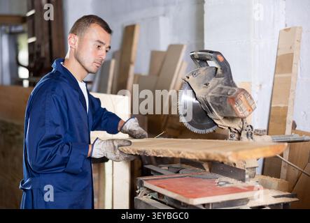 Young man saws oak plank in workshop Stock Photo