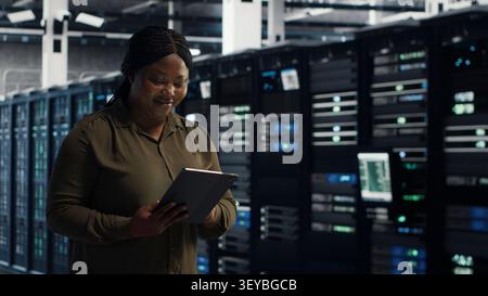 Systems engineer with digital tablet walks through server facility rows of servers, rolling out advanced power management solutions. Stock Photo