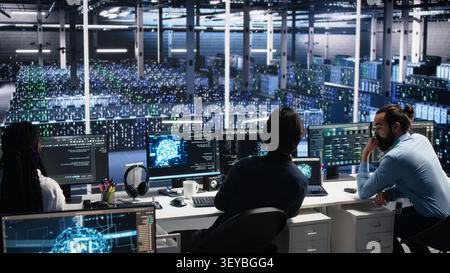 Server room system administrators working with AI to check digital infrastructure diagnostics with IT professionals in server facility assessing operational performance data using AI tools. Stock Photo