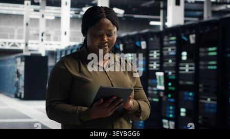 Technical specialist working with digital tablet in server facility, integrating new technologies and systems. Stock Photo