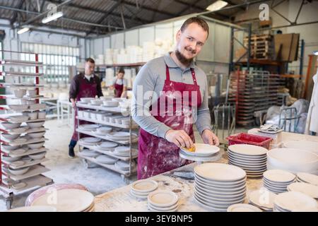 Skilled artisan cleaning plates with sponge in ceramics studio Stock Photo