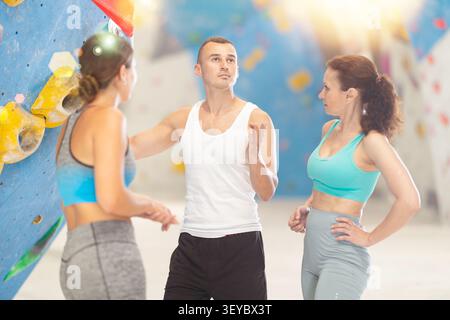 Athletic man and two sporty women discussing climbing options near climbing wall Stock Photo