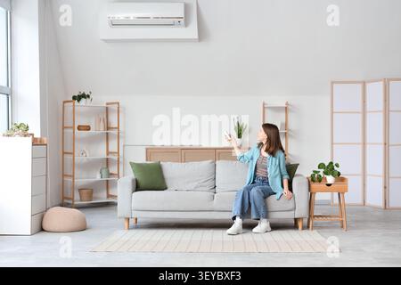Woman controlling air conditioner with remote in living room Stock Photo