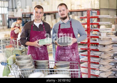 Two potters holding handcrafted ceramic plates in pottery workshop Stock Photo