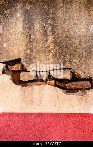 Exposed Brick Layers Under Broken Plaster Texture on Weathered Wall - Close-up of a damaged and cracked concrete wall showing exposed inner bricks and Stock Photo