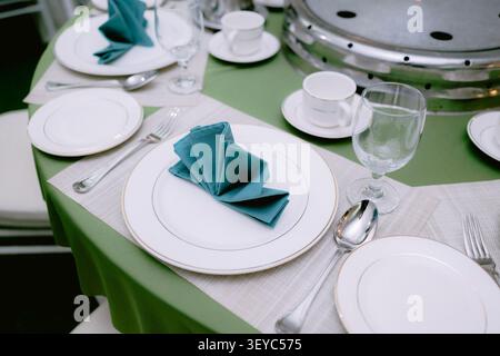 Elegant wedding reception table setting with white plates, green folded napkin, cutlery and glassware. Stock Photo