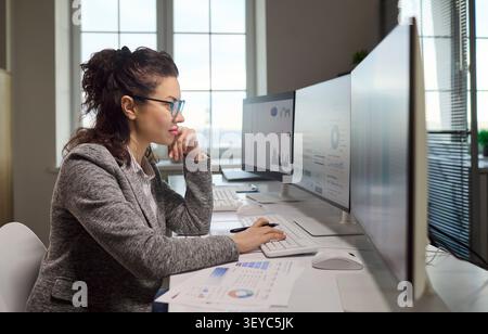 Female accountant analyzing financial data on computer monitors with spreadsheets Stock Photo