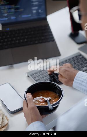 Adult Man Eating Lunch While Working on Computer in Office Stock Photo