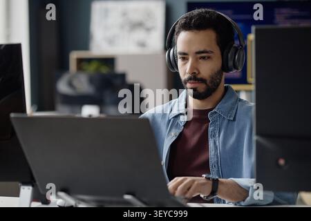 Adult Man Wearing Headphones Working on Laptop in it Office Stock Photo