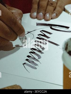 Close-up of a calligrapher creating modern hand lettering with a dip pen and black ink on white paper during a calligraphy practice session. Stock Photo