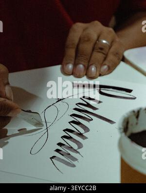 Close-up of a calligrapher creating modern hand lettering with a dip pen and black ink on white paper during a calligraphy practice session. Stock Photo
