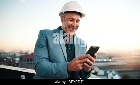 Typing, man and architect with phone, sunset and engineering for urban infrastructure outdoor. Communication, mature person and contractor on rooftop Stock Photo
