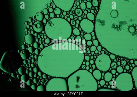 Closeup view of green illuminated bubbles and foam cells suspended in liquid, creating organic microscopic texture with dark outlines and scientific abstract Stock Photo