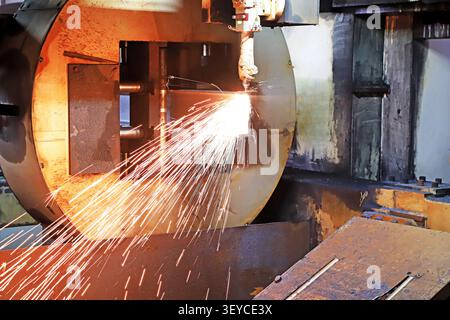 Dynamic close-up of a CNC plasma cutter slicing through a large steel plate, creating a dramatic burst of bright orange sparks. This high-precision in Stock Photo