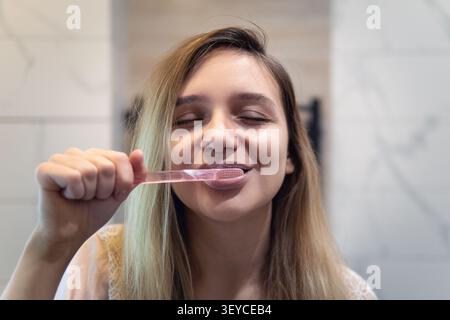 A woman is carefully brushing her teeth while standing in front of a mirror, ensuring her oral hygiene is maintained properly Stock Photo