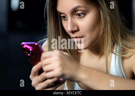 Girl texting on the smart phone indoor home and she is shocked. Blonde woman use her pink smartphone. Shocked bad news Stock Photo