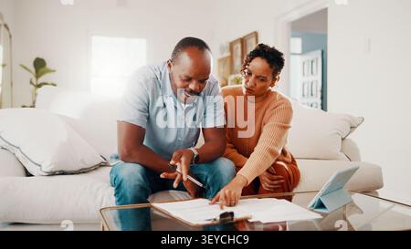Documents, discussion and couple on sofa in home with budget planning, savings or bills review. Reading, paperwork and African man with woman for Stock Photo