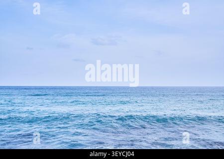 Minimalist coastal landscape featuring gentle turquoise waves and a soft pastel sky. Offers expansive empty space for seasonal design layouts. Stock Photo