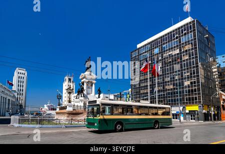 A vintage green trolleybus passes the Monument to the Heroes of Iquique at Plaza Sotomayor in Valparaiso, Chile. Stock Photo