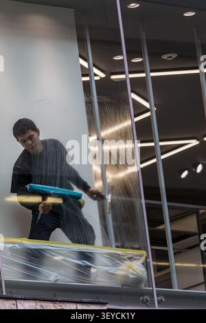 Osaka, Japan April 23, 2026 A worker cleans large glass windows inside a modern commercial building, maintaining cleanliness and visibility in a profe Stock Photo