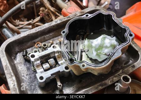 An engine part disassembled on metal tray with various bolts and nuts scattered around, showing mechanical components and oily surfaces in workshop se Stock Photo