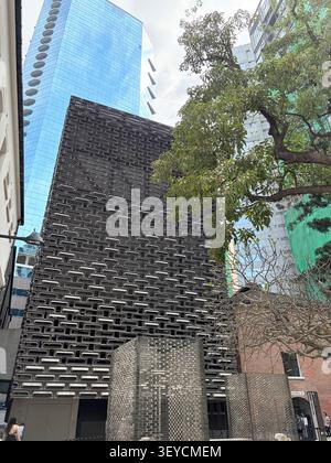 Low-angle view of a striking patterned dark facade building contrasting with a glass skyscraper and tropical trees in an Asian city center. Stock Photo