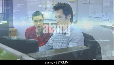 Team sitting at desk, man typing and activating HUD while woman leaning and analyzing tech data Stock Photo