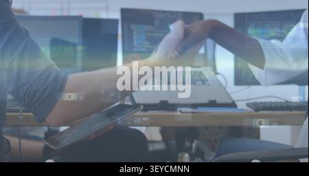 Tech devs reaching across desk shaking hands over code screens overlay covering hands sealing deal Stock Photo