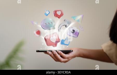 Cropped hand holding smartphone with floating 3D social media icons for digital marketing and online communication Stock Photo