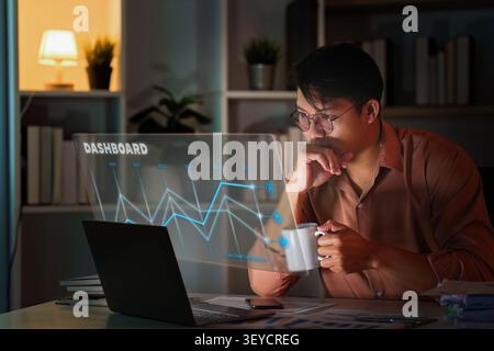 Asian man analyzing data on holographic dashboard in home office for business intelligence Stock Photo