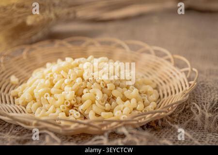 Dry Elbow Macaroni Pasta in Wicker Basket on Rustic Linen Background Stock Photo