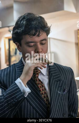 Portrait of a young man dressed in a sharp dark pinstripe suit, smoking a luxury cigar . Stock Photo