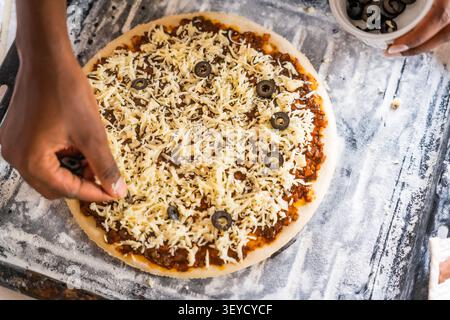 young african woman hands making pizza on table in kitchen for recipe concept, homemade food preparation and livelihood and employment in africa Stock Photo
