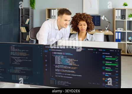 Developers pair programming and reviewing code on monitors in modern office Stock Photo