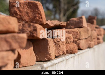 Uneven red stones, freshly dug from the ground, are arranged in neat rows and stacked on top of each other. The rough texture and earthy tones Stock Photo