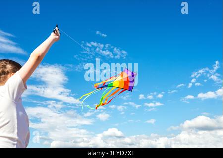 Teen boy flying a colorful kite beneath a blue sky Stock Photo