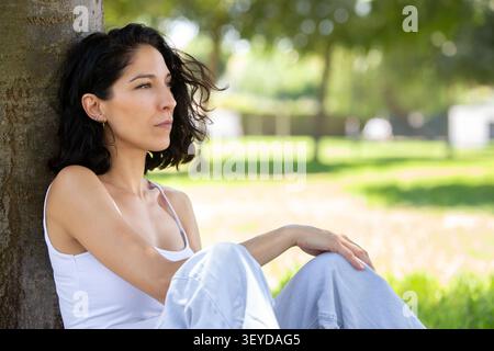 Thoughtful young woman sitting under a tree in a peaceful park Stock Photo