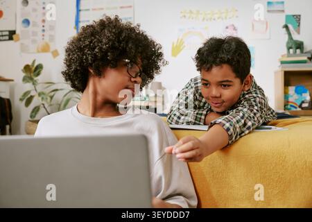 Black Teenager Tutoring Boy While Using Laptop at Home Stock Photo