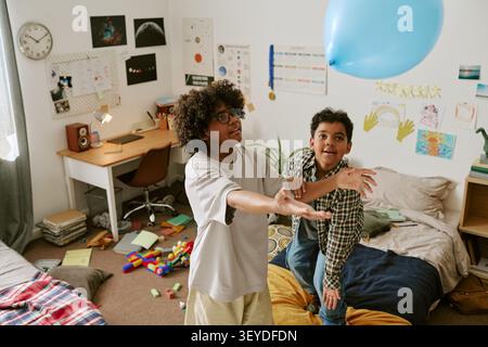 Black Boys Playing with Balloon in Bedroom during Home Leisure Stock Photo