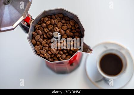 A coffee cup and a red coffee pot containing coffee beans on a white table Stock Photo