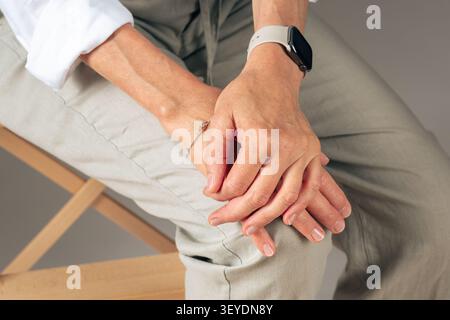 Hands clasped together, in indoor on a chair, with bracelet, watch, with fabric, metal texture, from a close-up from above perspective, with white Stock Photo