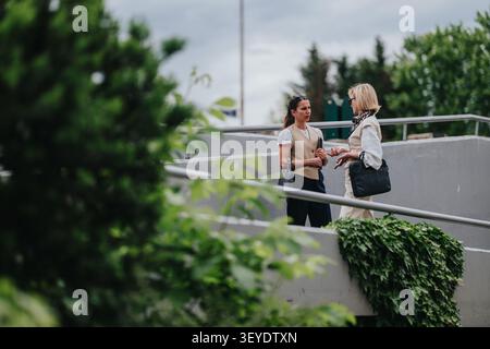 Two businesswomen having a conversation on an outdoor ramp surrounded by greenery during daytime Stock Photo