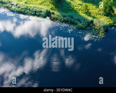Aerial view of a small boat on the calm waters of the Bullupe River near Kleisti, creating ripples in the water, surrounded by lush green riverbanks i Stock Photo