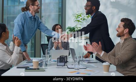 Multiethnic business team at office conference African American and Caucasian businessmen shaking hands group of colleagues applauding boss showing Stock Photo