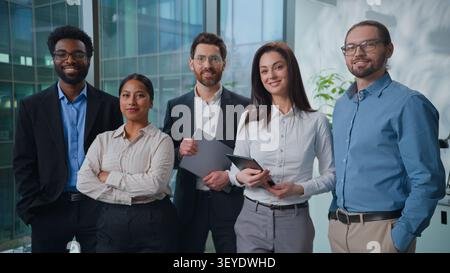 Happy multiethnic business team posing in office together. Five multiracial businesspeople colleagues smiling looking at camera at company. Cheerful Stock Photo