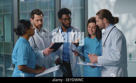 Group of five multiracial medical doctors emotional talking with digital tablet device papers documents medicine results. African American leader Stock Photo